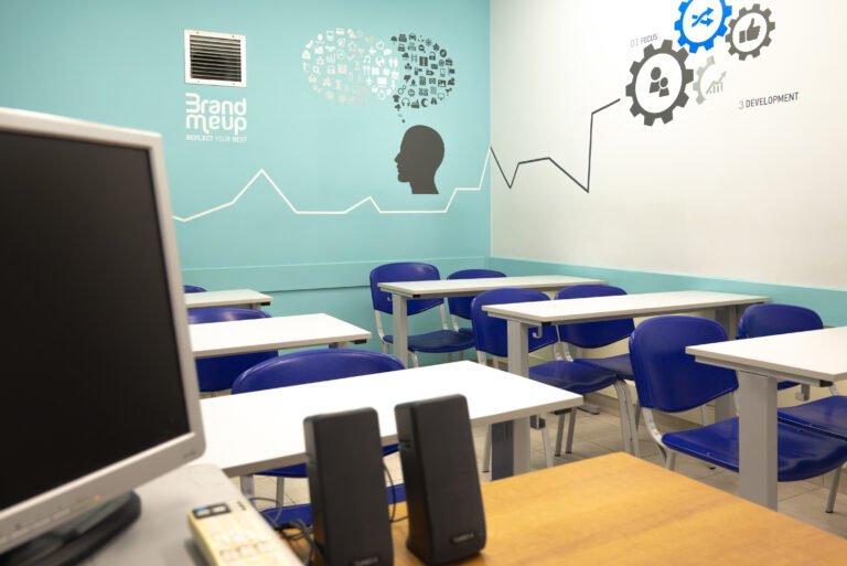 Bright classroom setup with blue wall illustrations, desks, and computer speakers.