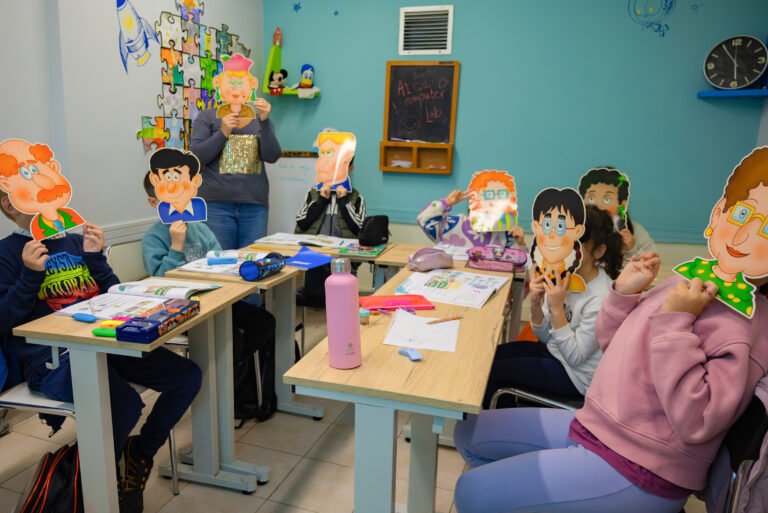 Students holding cartoon face masks while participating in a fun educational activity in a classroom.
