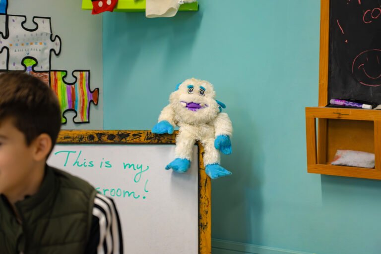 Whiteboard with handwriting and a plush toy used for young learners' classes.